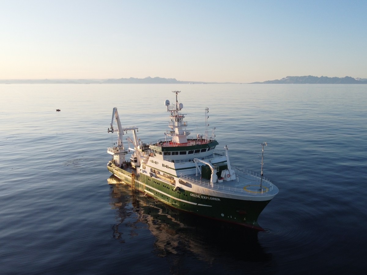 A green and white boat on a calm sea.