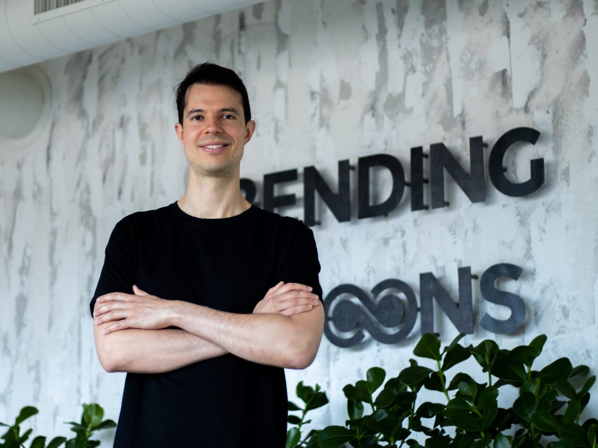Caucasian man in black tee, Bending Spoons logo behind on wall.