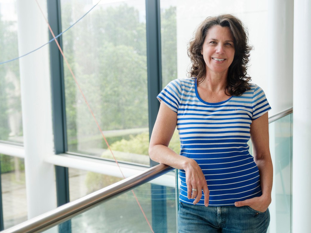 A woman with brown hair in a blue t-shirt and jeans, smiling.