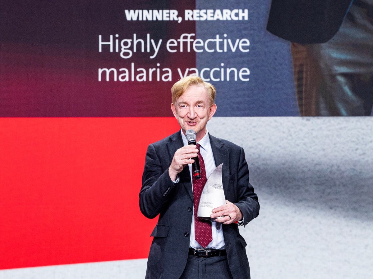 A middle age white man with fair hair, in a suit and holding a microphone.