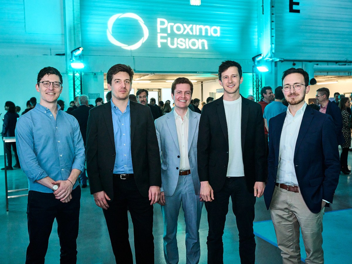 Five men all wearing suits stand together smiling in front of a wall with Proxima Fusion