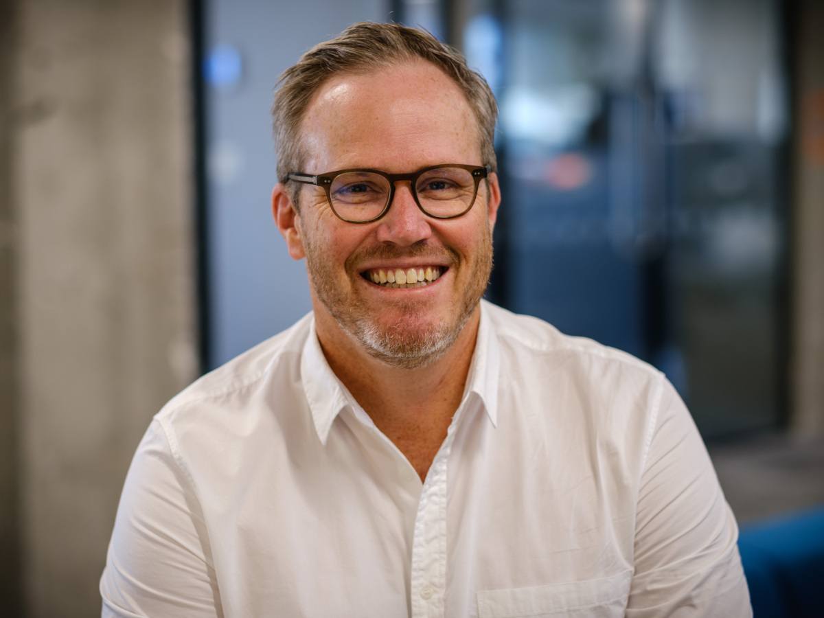 A man in a white shirt and glasses, smiling at the camera