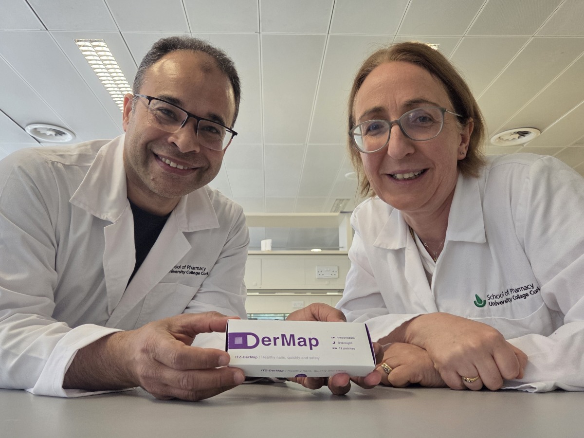 A man and woman in a lab wearing lab coats and glasses pose with packaging for the treatment they are developing.