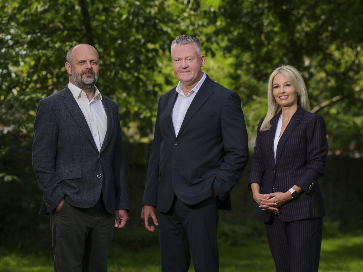 Two men and a woman in business attire posing in an outdoor setting.