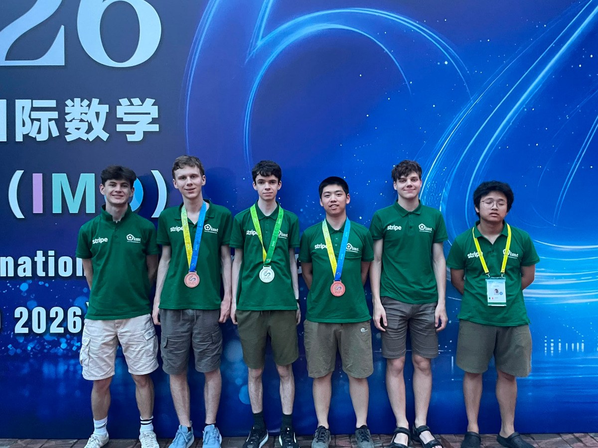 Six racially diverse teenage boys in Green shirts, showcasing bronze and silver medals, in front of a blue background.