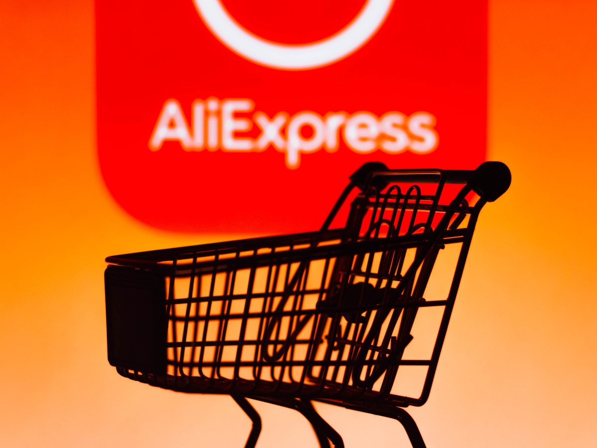A picture of a shopping cart sat in front of an orange wall with the AliExpress logo on it.