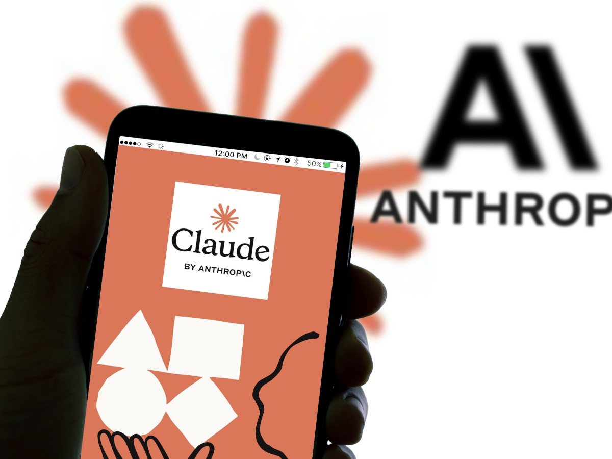 The Claude website opened on a smartphone in the foreground. Anthropic’s logo in the background.