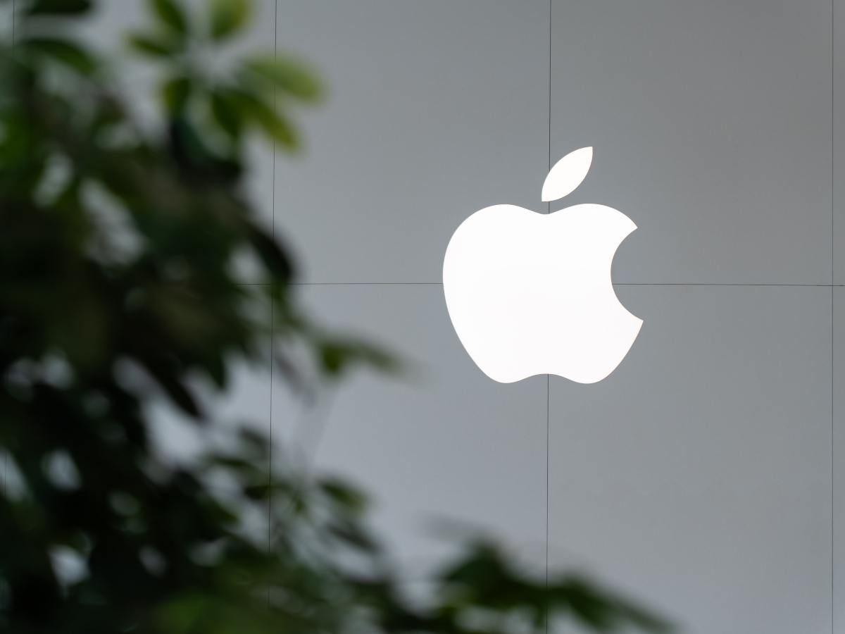 The Apple logo on a glass building, with the reflection of a tree on the building.