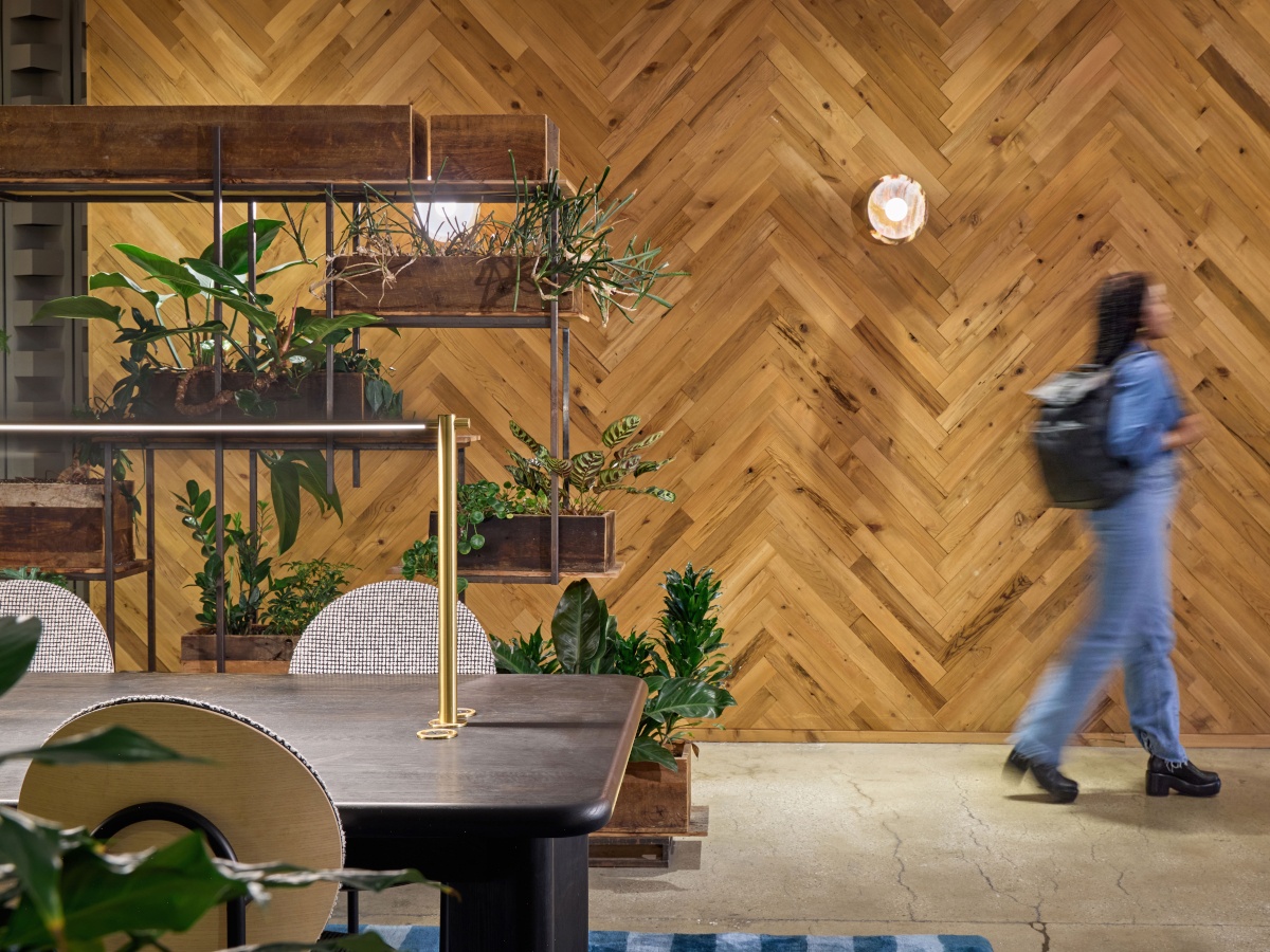 A wood panelled office setting with a desk, plants, and an employee walking.
