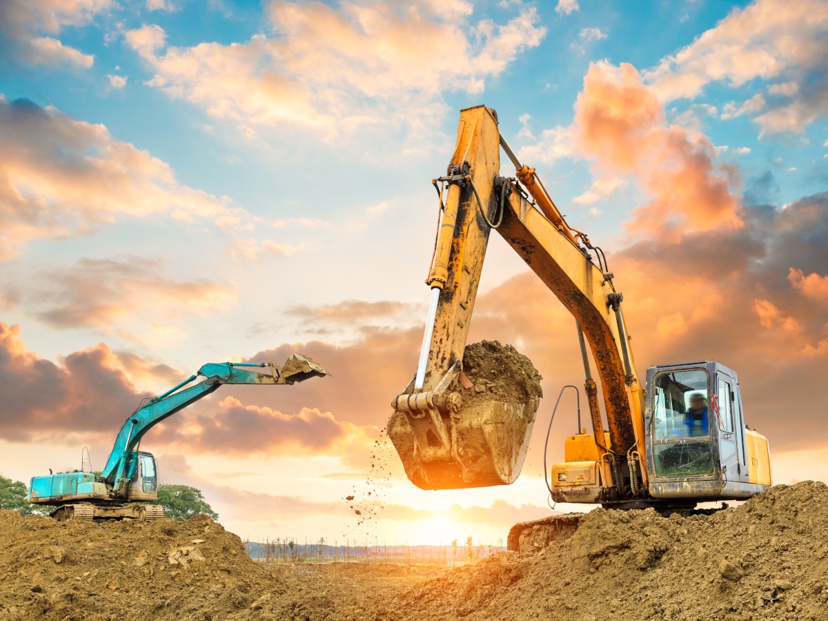 Two diggers moving earth in front of a sunset.