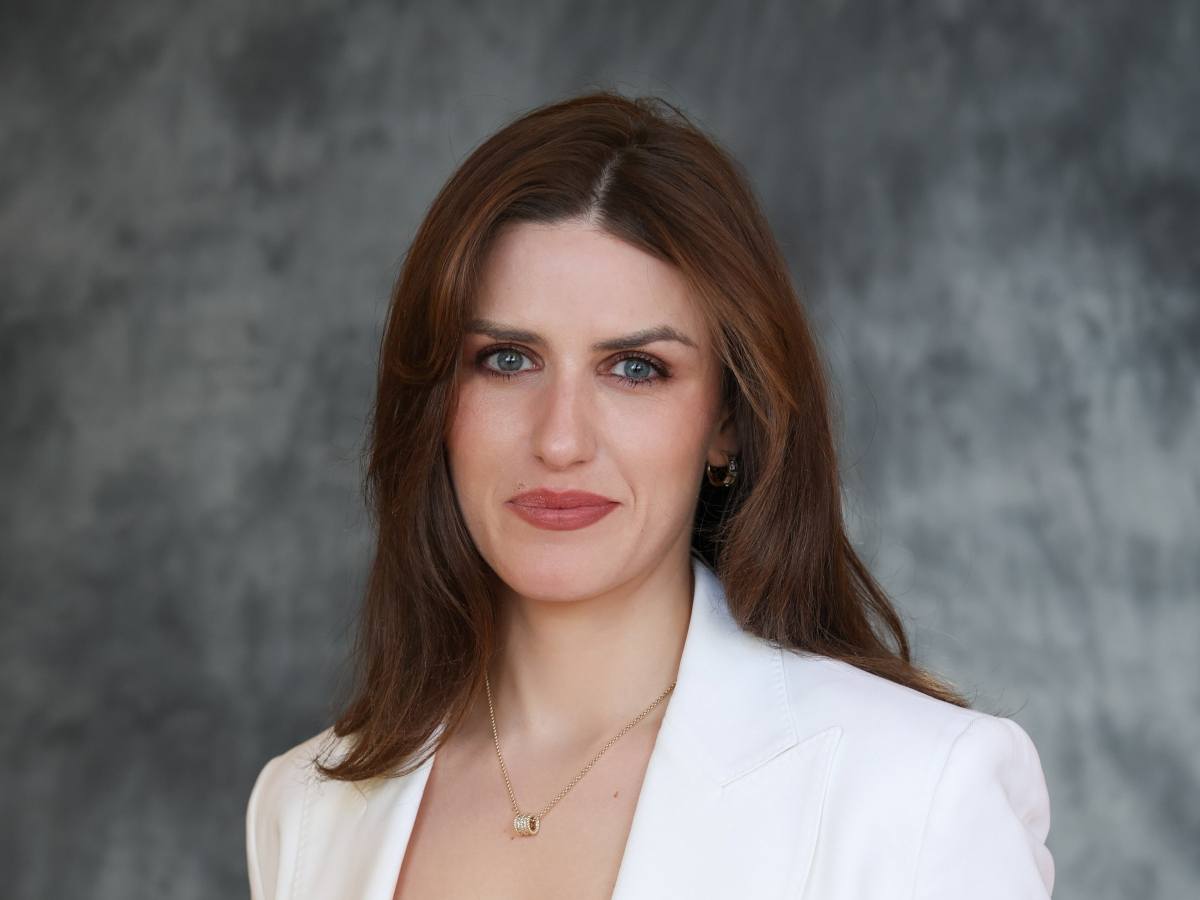 Headshot of a white woman with dark hair wearing a white blazer in a portrait setting.