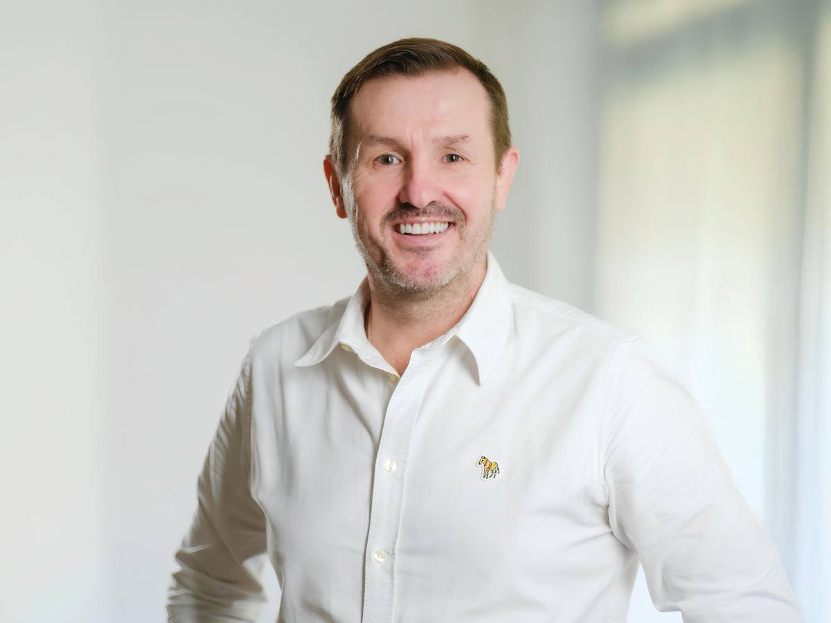 A white man with red hair and beard in a white collared shirt smiles for the camera.