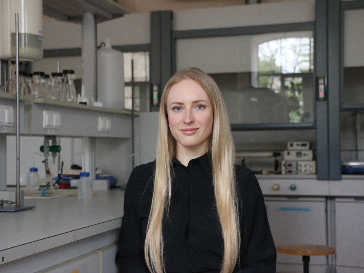 A young white woman with long blonde hair in a black jumper, sitting in a lab.