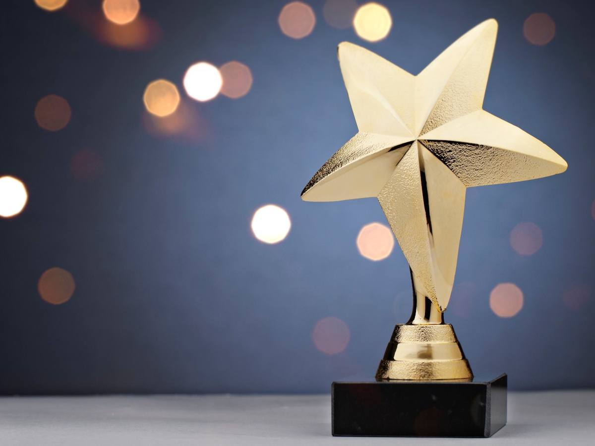 A gold star-shaped trophy against a blurred glittery background.