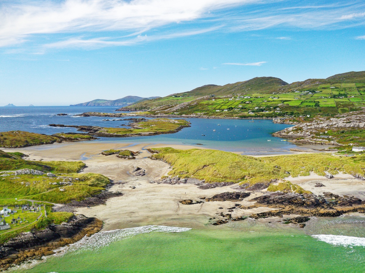 A picture of a Derrynane beach in Kerry, with a bay featured behind with mountains in the backdrop on a sunny day.