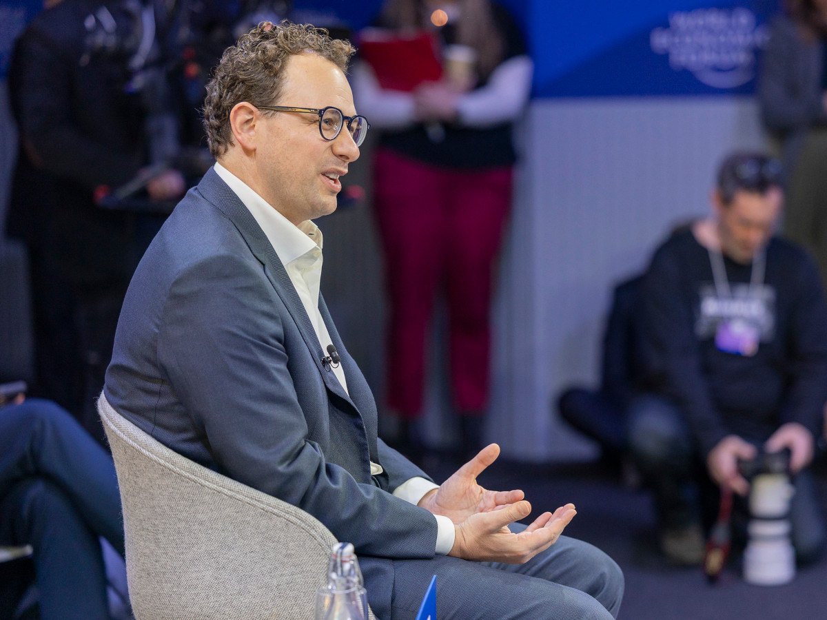 The side profile of a man in a suit with glasses sitting on a chair.