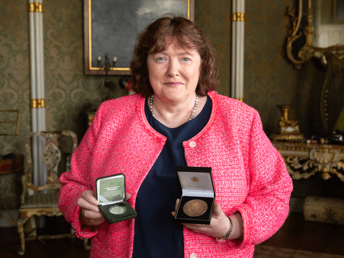 A woman in a pink jacket holding two medals.