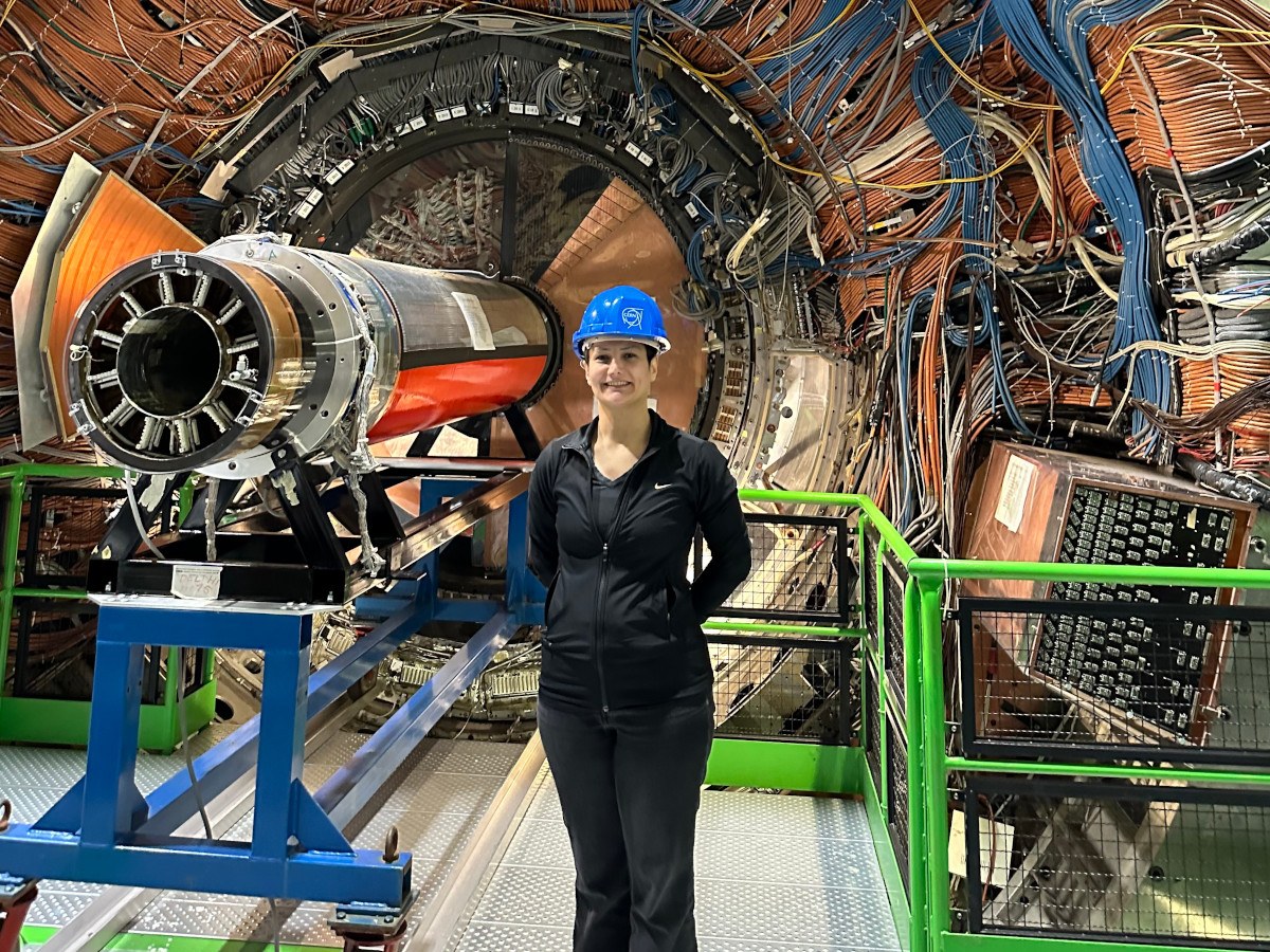 A person wearing black clothes with a blue hard hat standing in front of a large machine at CERN.