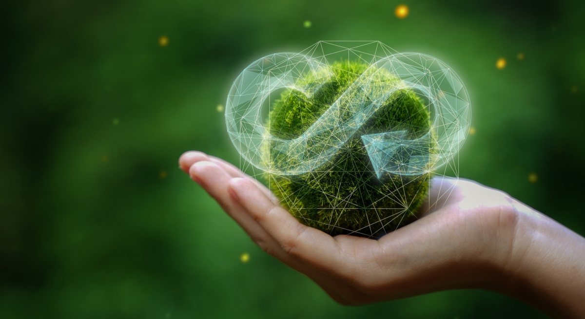 A hand holding up a grass world with a circular economy icon over it.