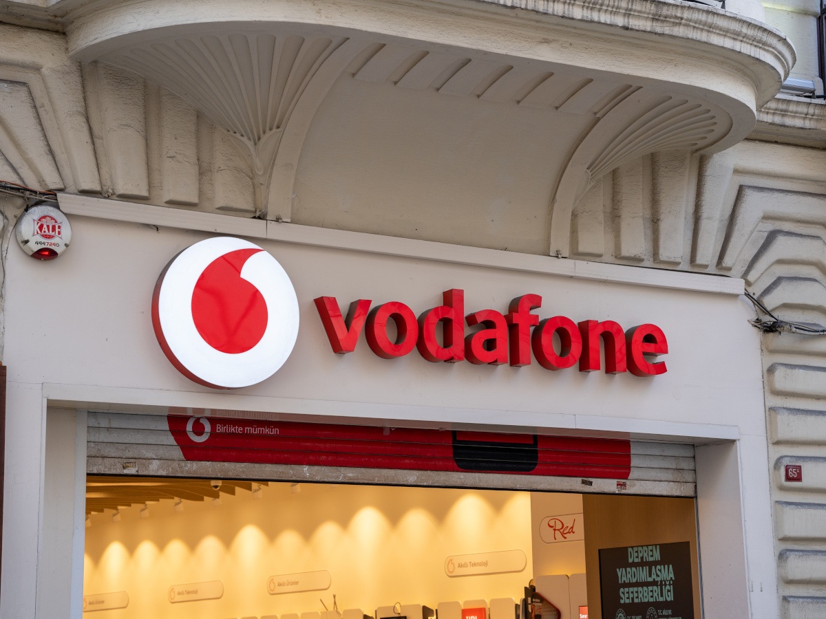 A Vodafone logo and sign on a cream building outside a shop.