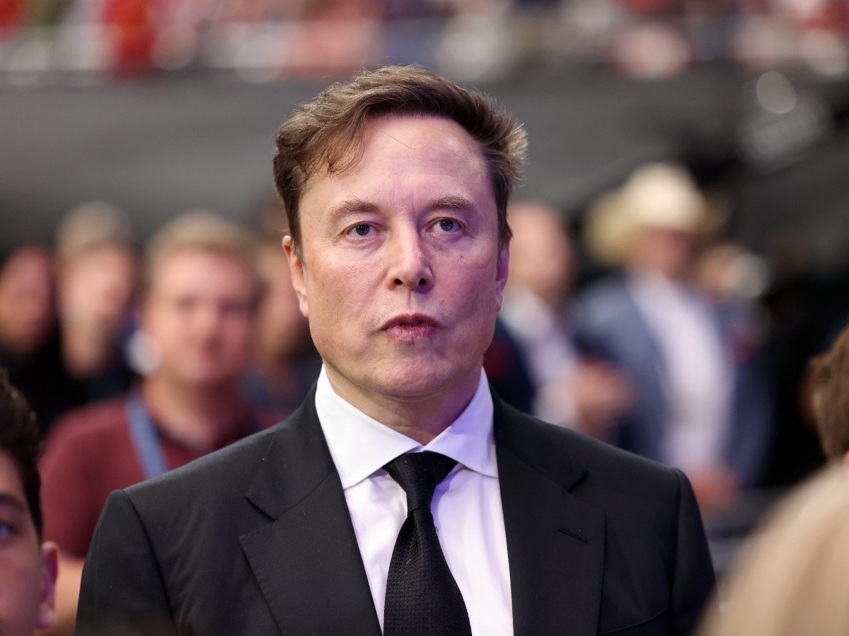 A man in a black suit and tie looking ahead. There