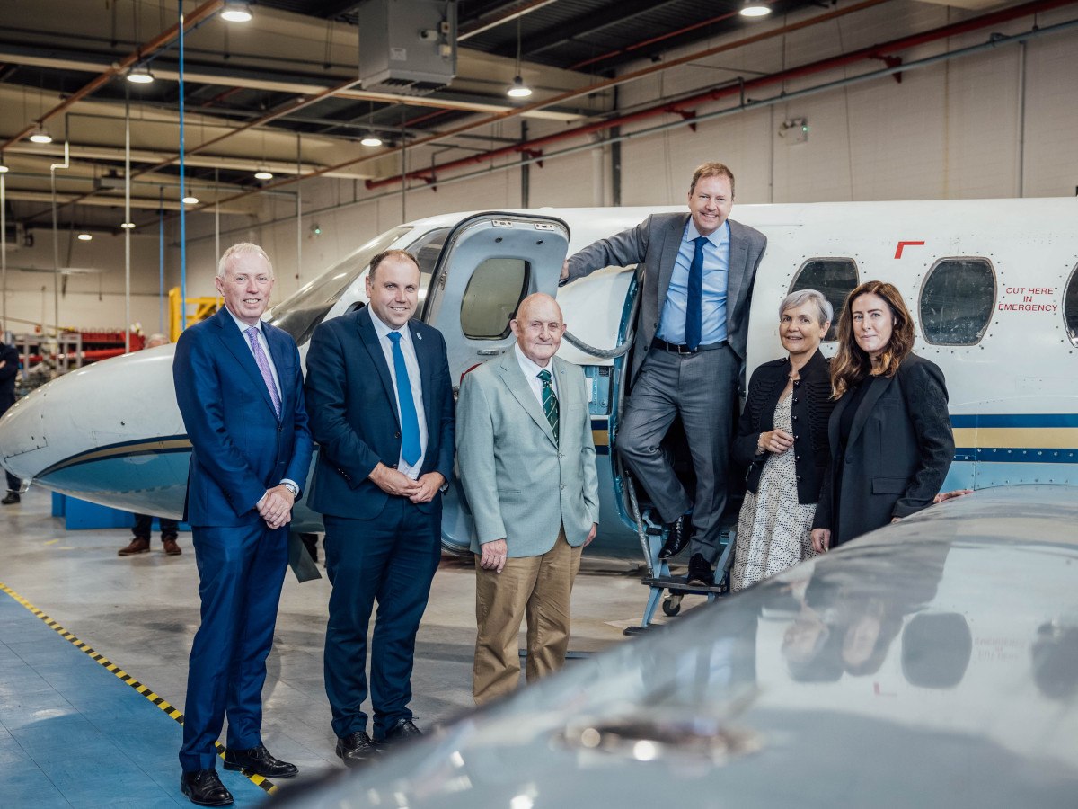 Six middle age adults in business attire in front of an aircraft.