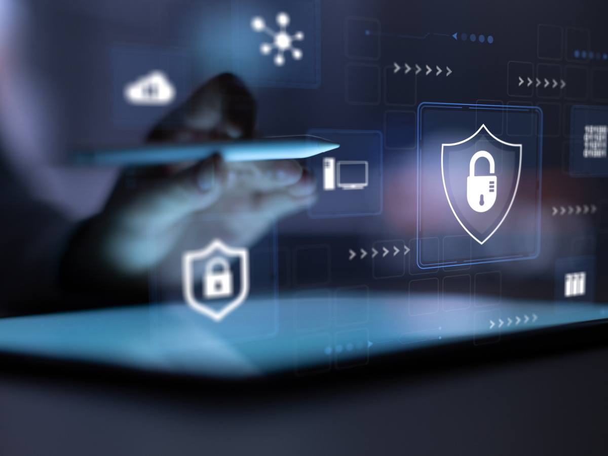 An unseen person holding a tablet pen over a tablet, with cyber icons around it.