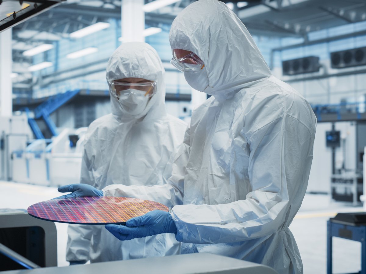Two people in white protective gear with masks and gloves holding a semiconductor wafer fab.