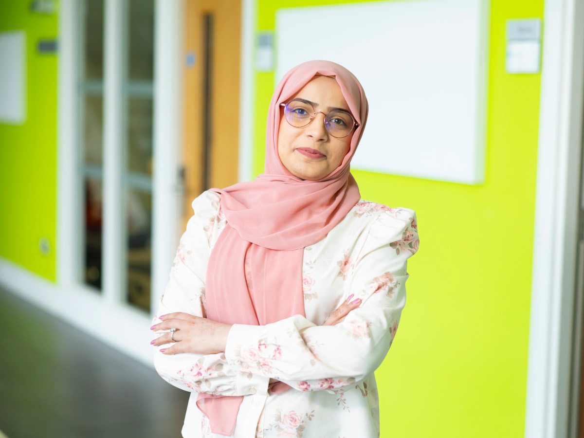 A woman in a pink hijab with glasses with her arms folded.