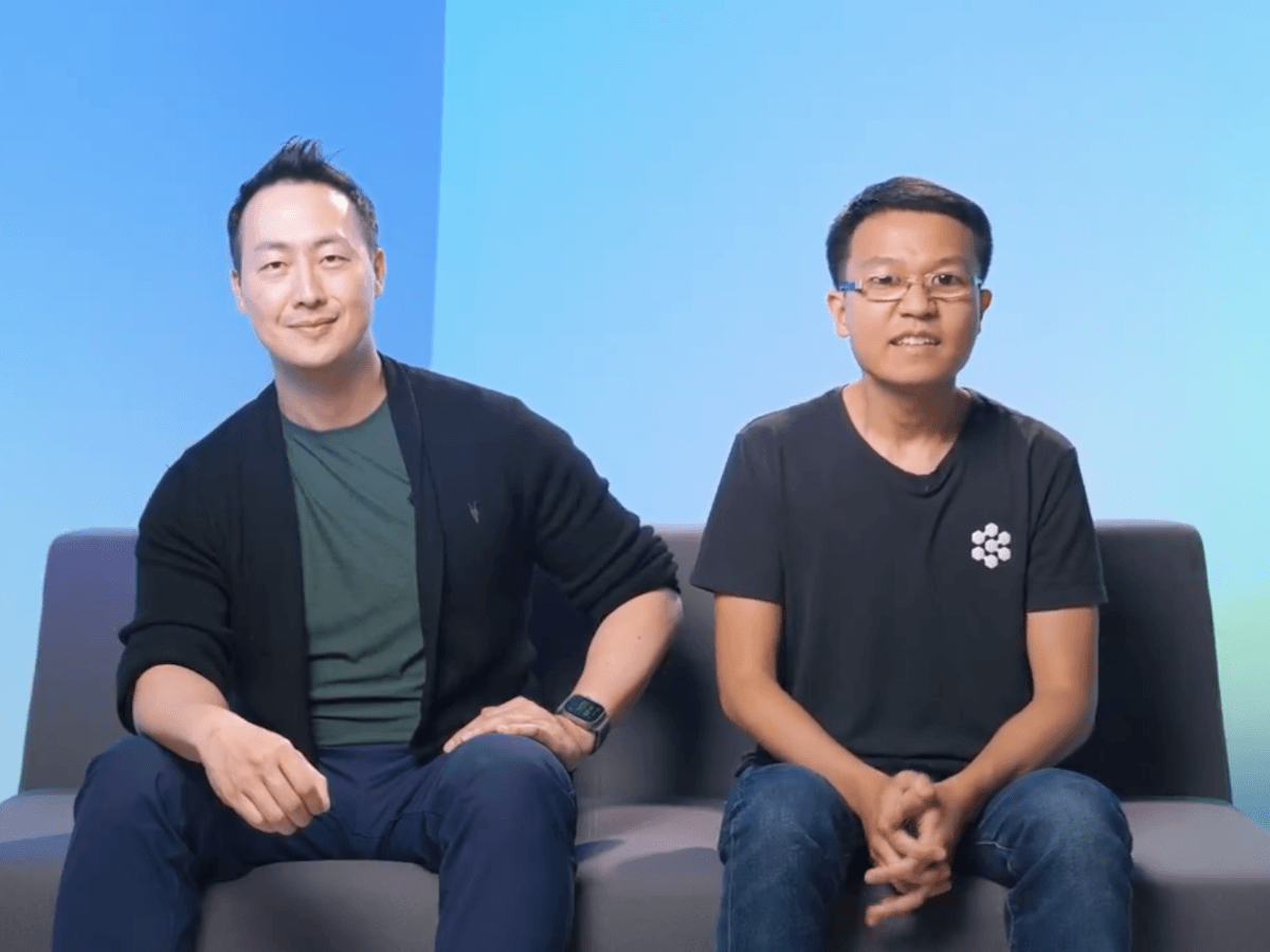 Image of two young men of Asian appearance, sitting on a couch with blue backdrop.