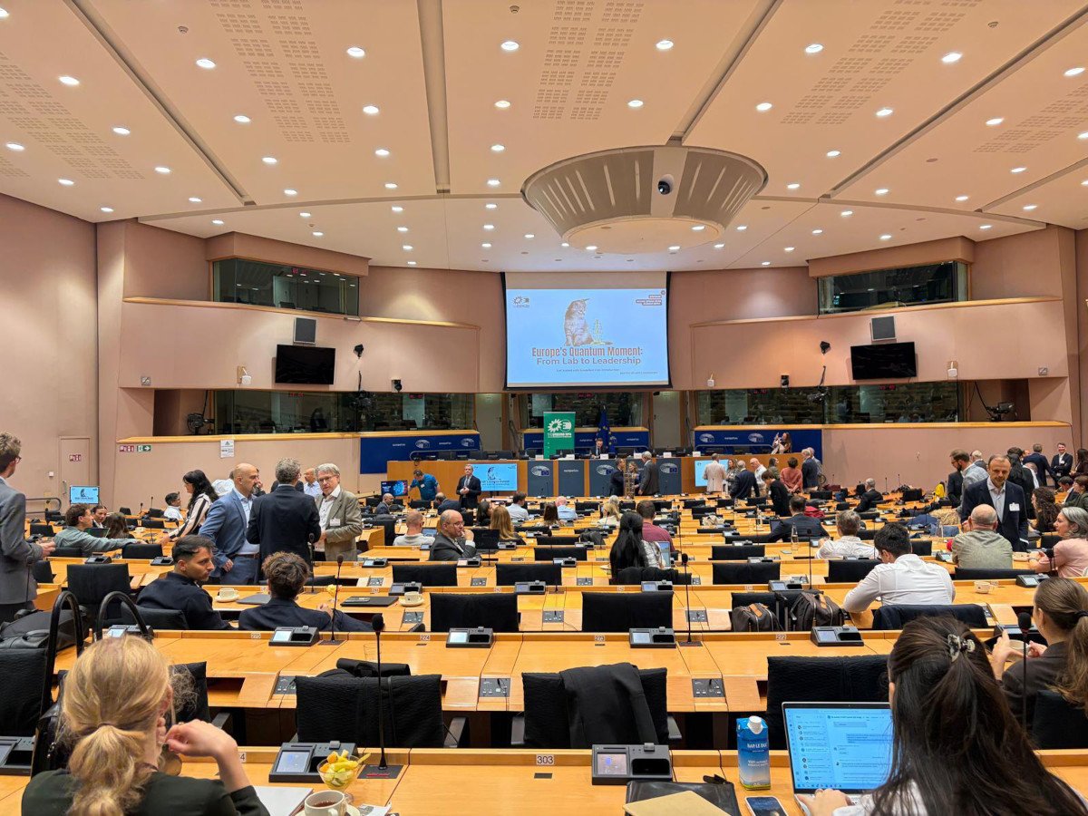 A large conference hall with computers and people seated at their desks.