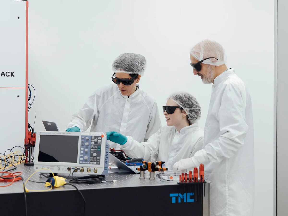 A group of people in white PPE and goggles examining a device on a desk.