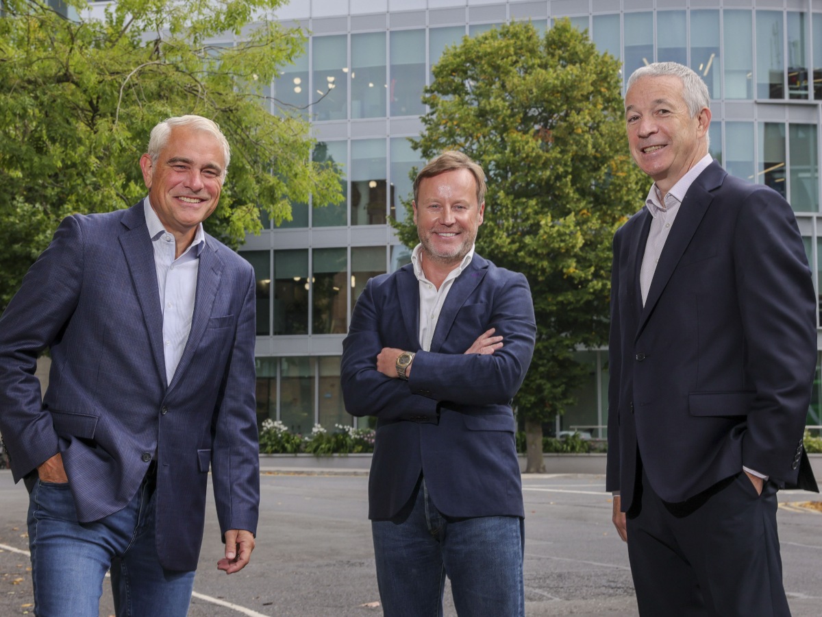 Three middle-aged white men in business attire standing in a row and smiling.