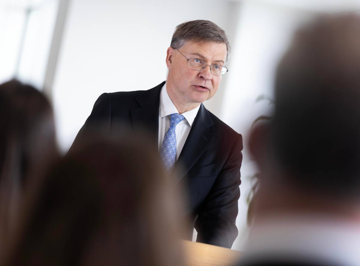 Caucasian male with suit and glasses addresses a small gathering.