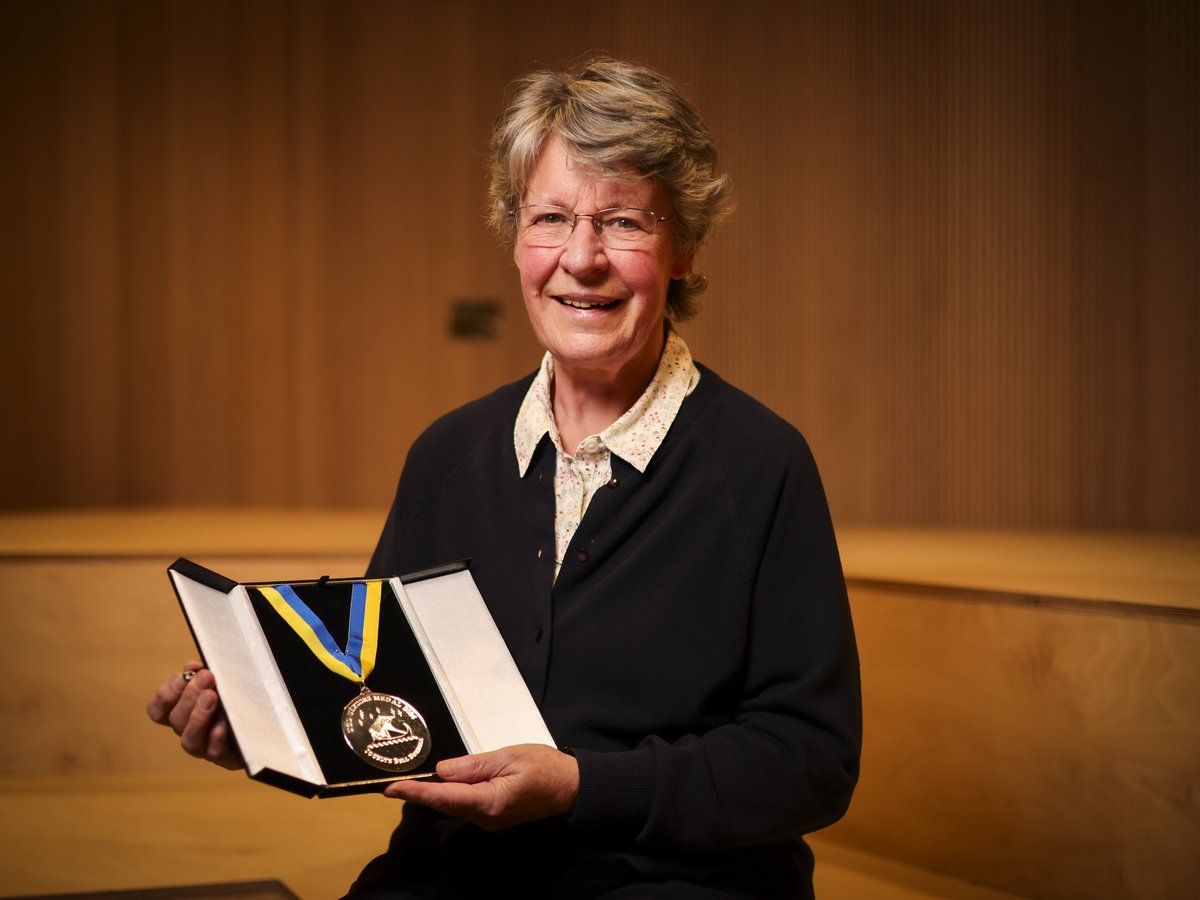 An older white woman in business casual clothes, holding a medal.