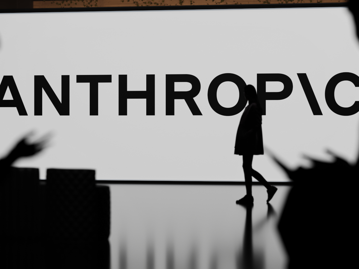 Anthropic logo on large screen, figures silhouetted in front.
