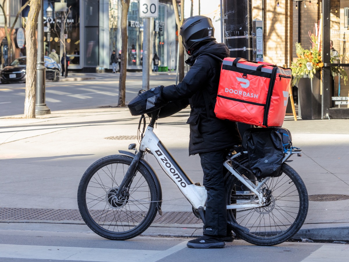 A delivery driver on a bike with a door dash bag on their back.