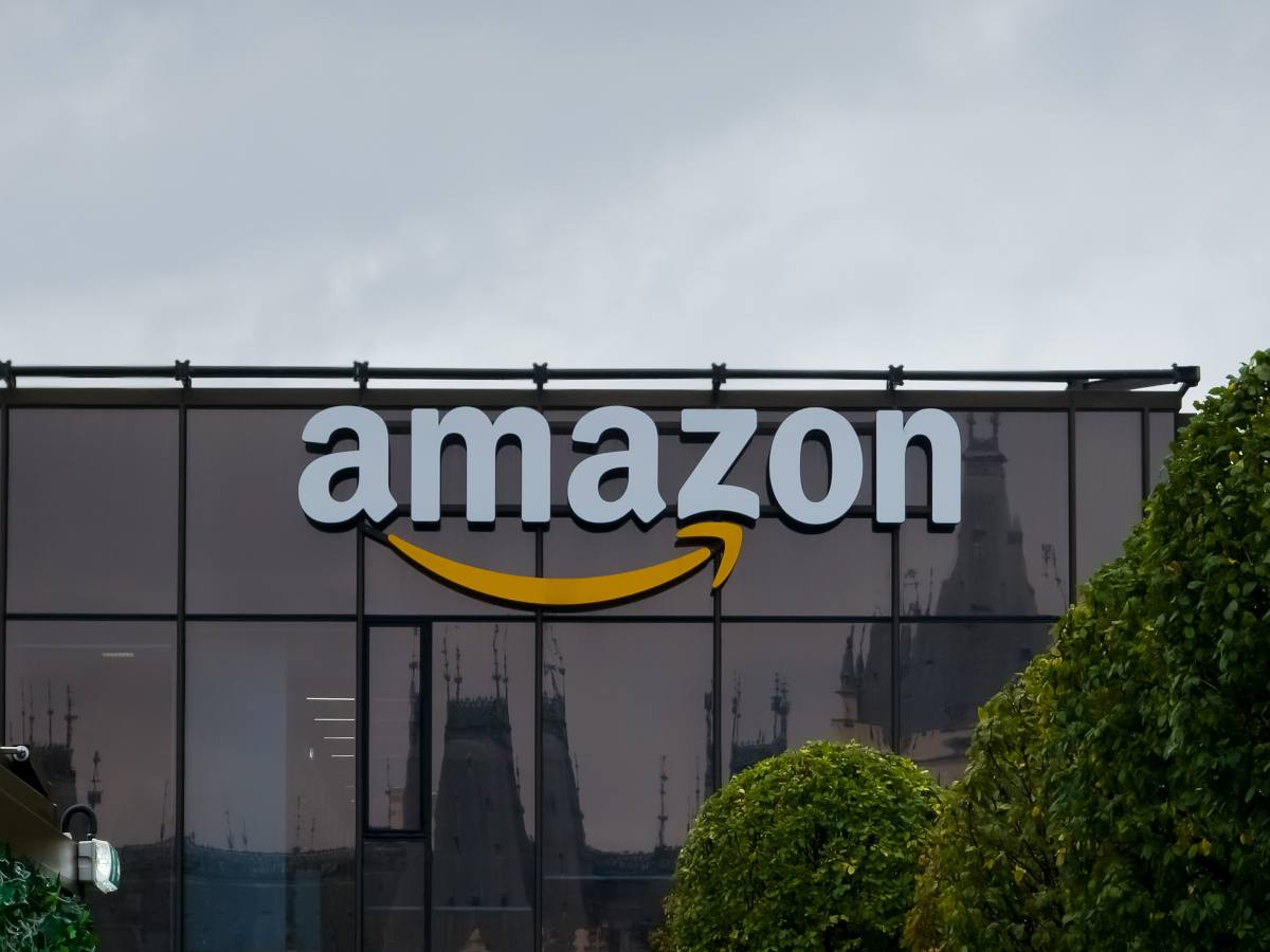 A picture of the Amazon logo on a glass office building at around midday, with clouds in the background.
