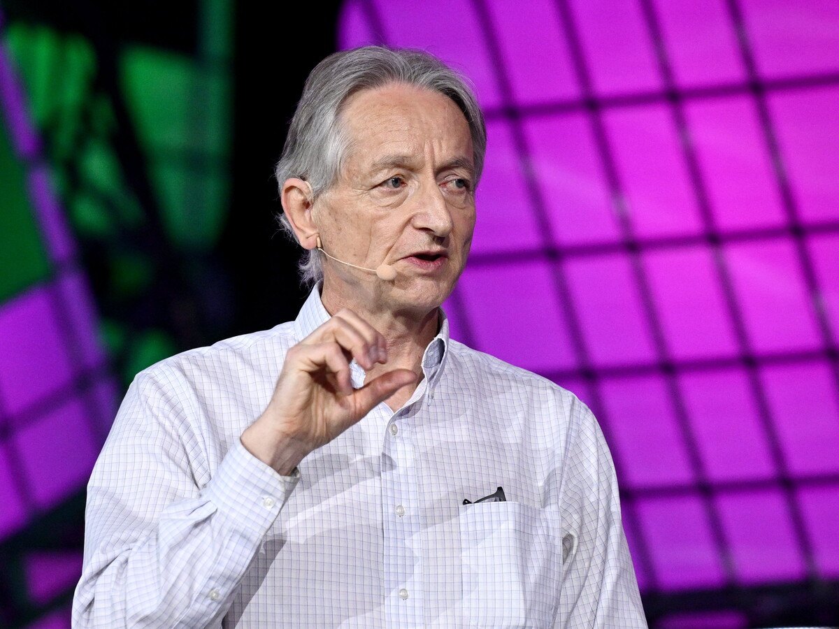 A man with grey hair and a light colour shirt standing on a vibrant stage, talking.