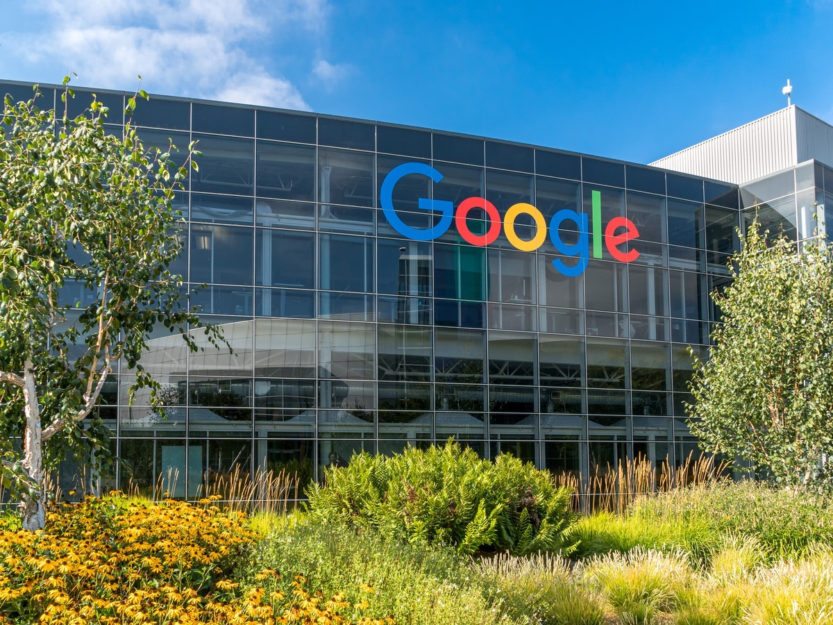 The Google logo on a glass building, surrounded by greenery and a blue sky.