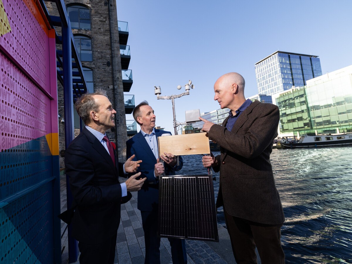 Three men in suits standing next to the Liffey river by a building talking.