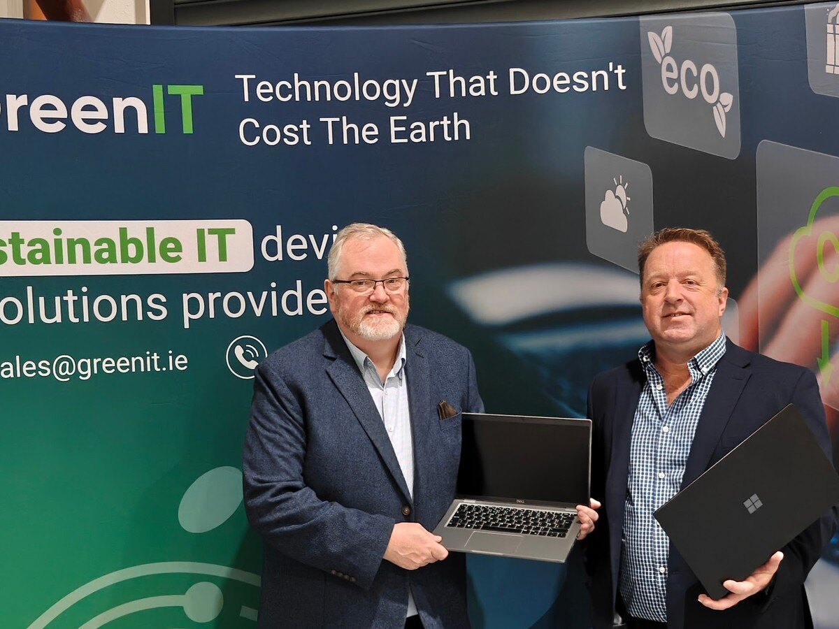 Two men wearing suits holding a laptop in front of a banner.