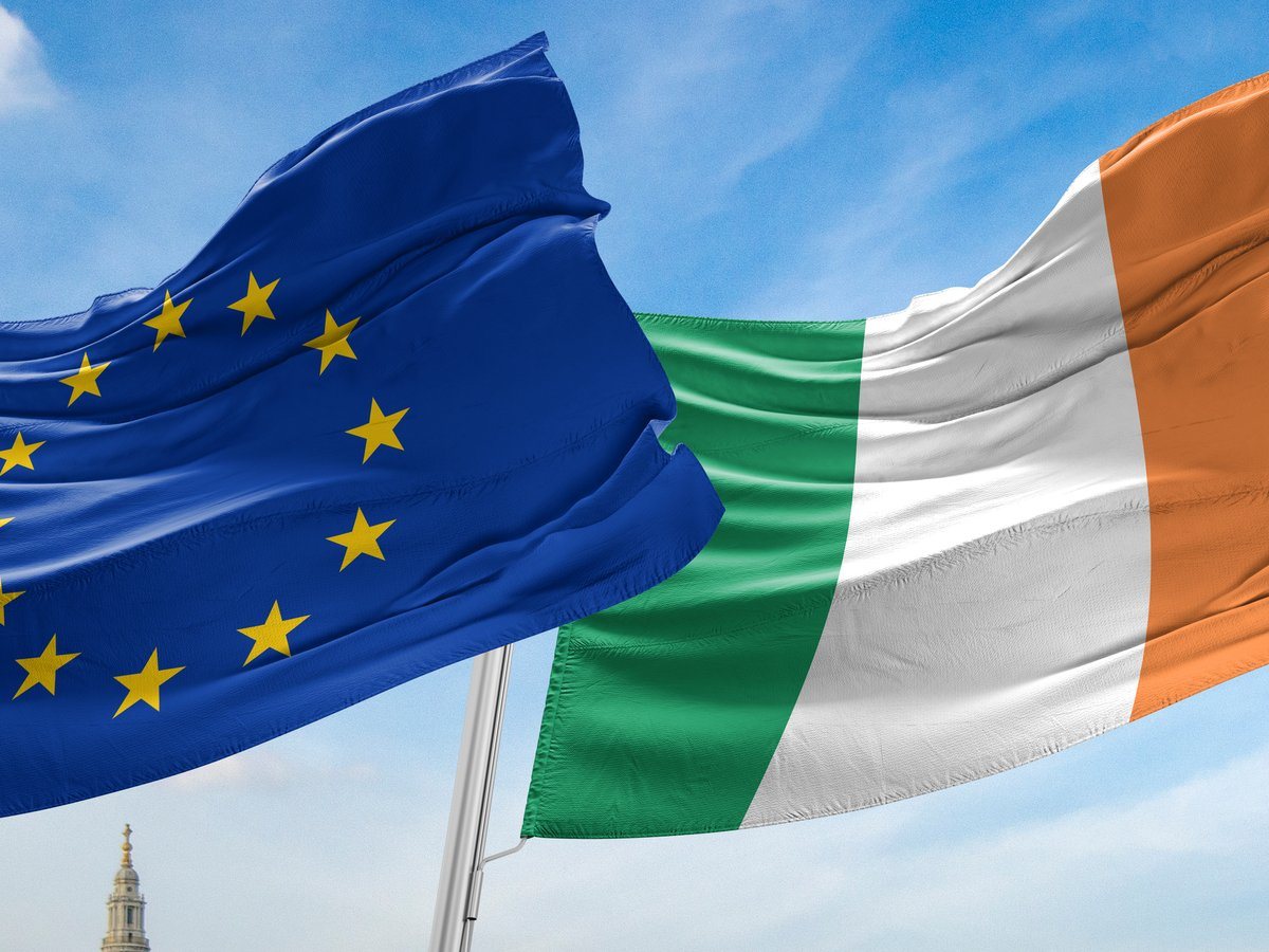 The European and Ireland flags blowing in the wind against a blue sky.