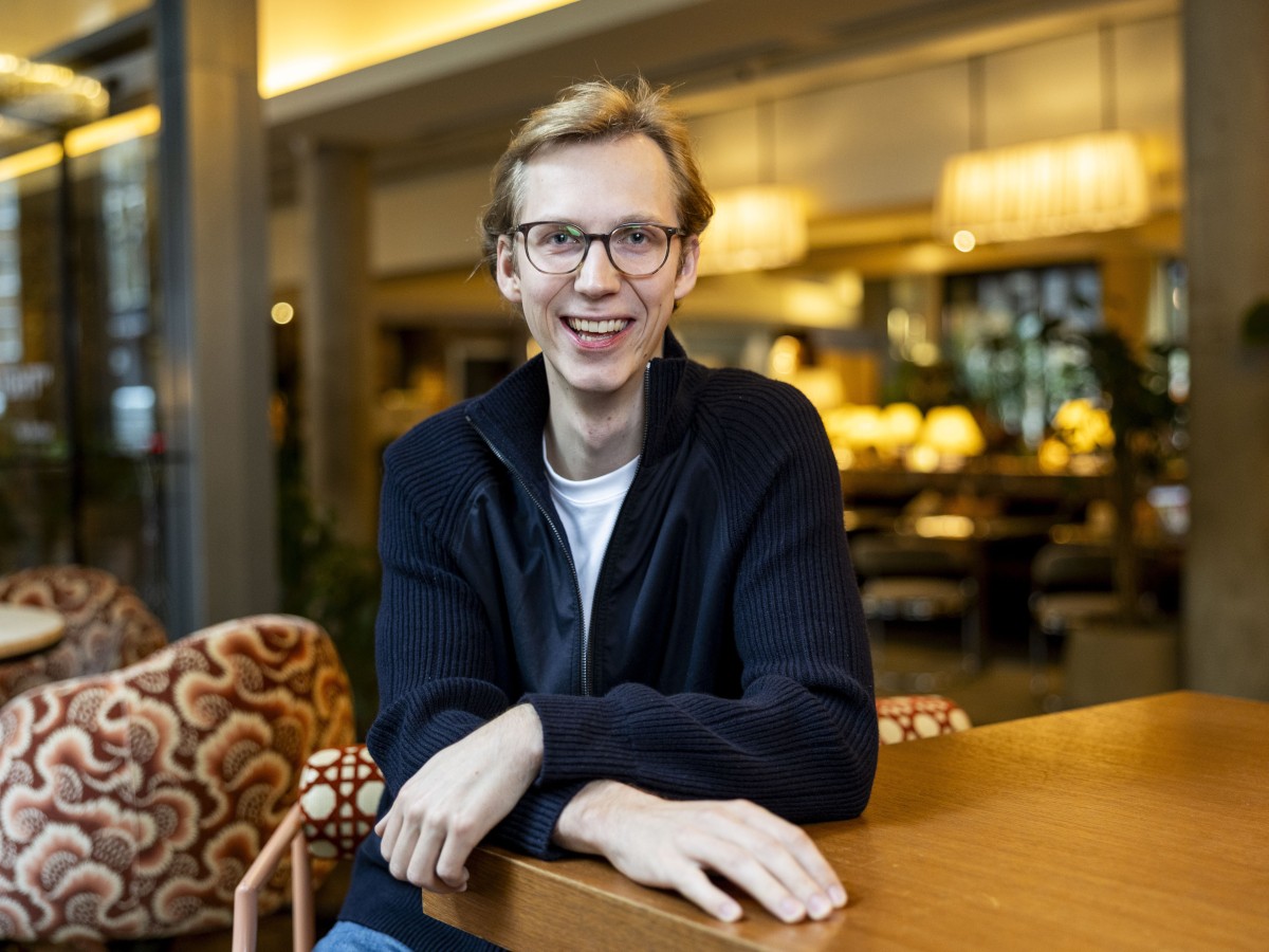 A white man wearing glasses smiles in front of a colourful office background.
