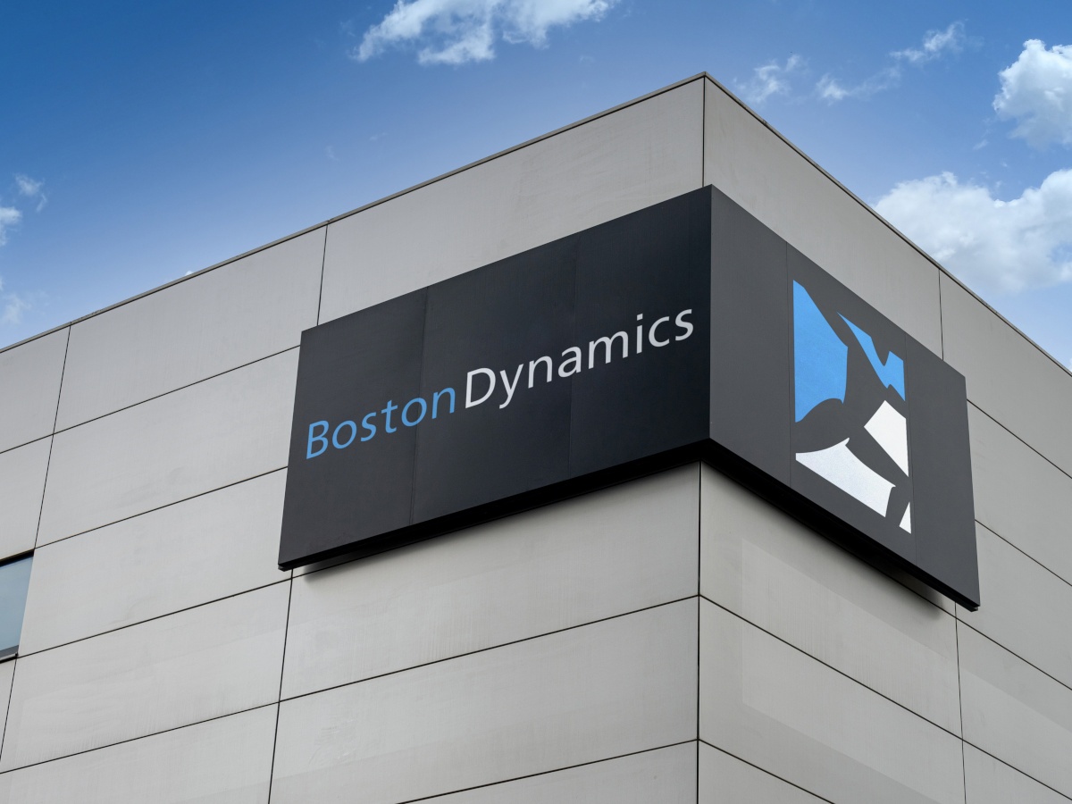 The Boston Dynamics logo on the corner of a stone building, against a blue sky background.