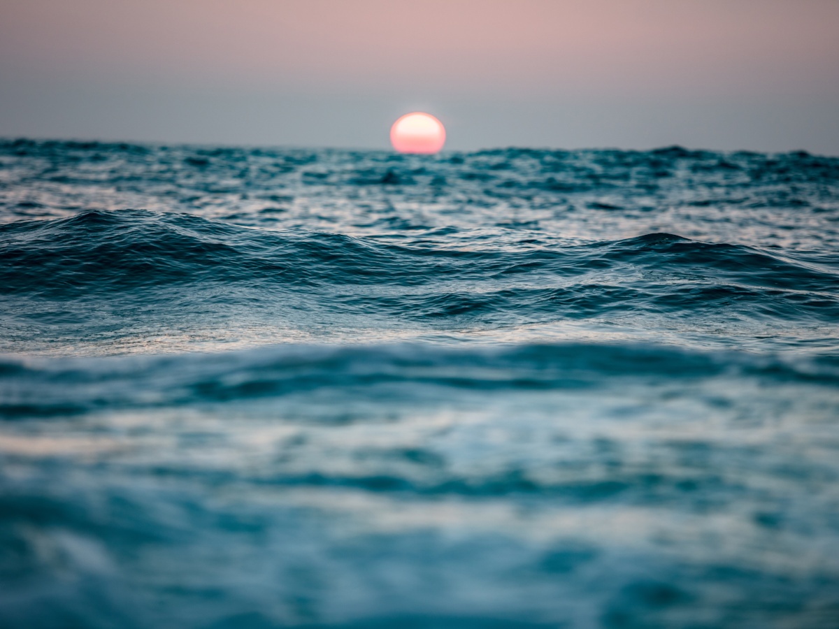 A picture of ocean waves in the late afternoon with a pink sun just setting on the horizon.
