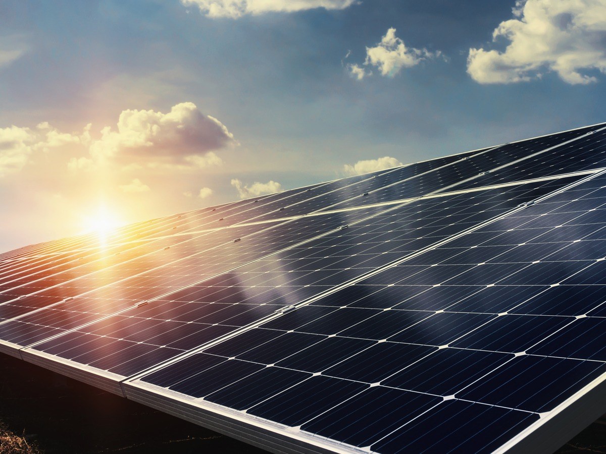An image of solar panels and a setting sun against a blue sky.