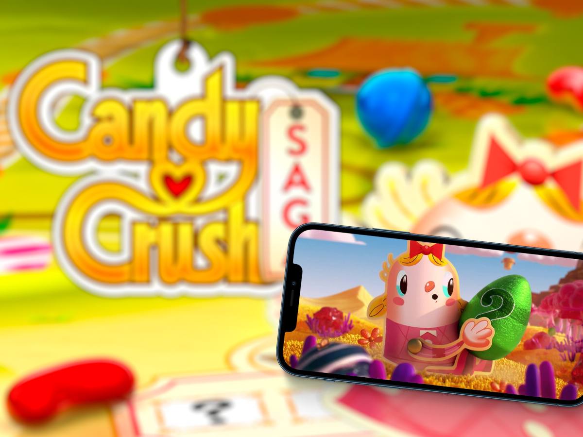 The candy crush saga game logo and design in the back with a smartphone showing the game in the foreground.